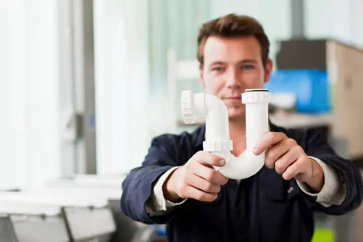 Apprentice plumber holding up waste pipe